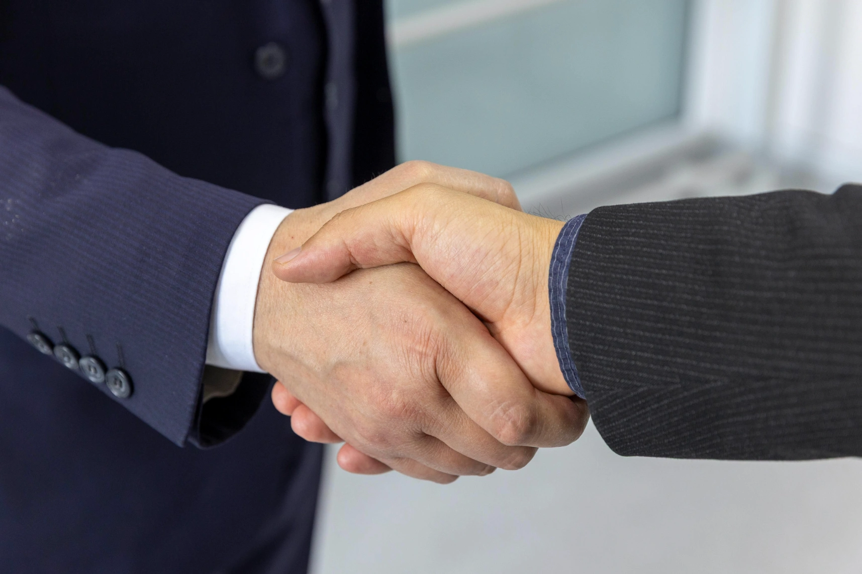 Two people shaking hands in a professional setting, representing partnership and collaboration.