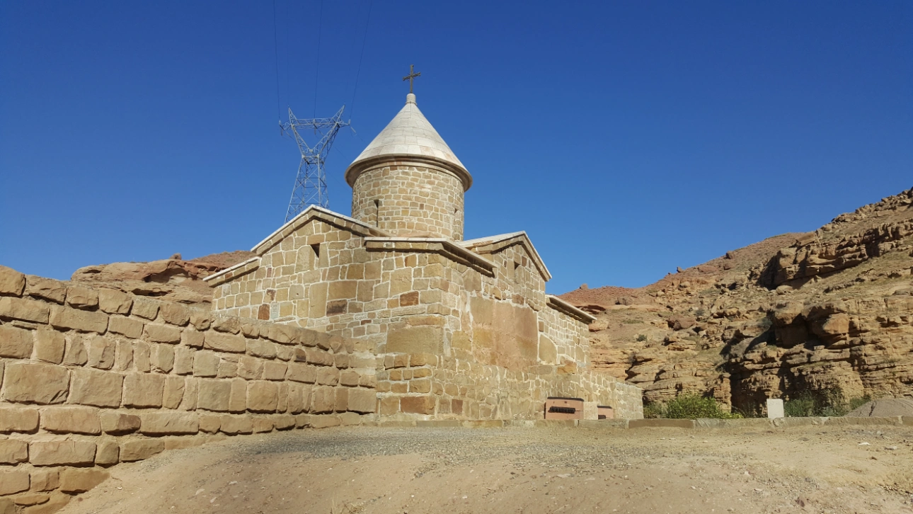 Stone Chapel of Chupan in Jolfa, Iran, set against a rocky landscape beneath a blue sky.