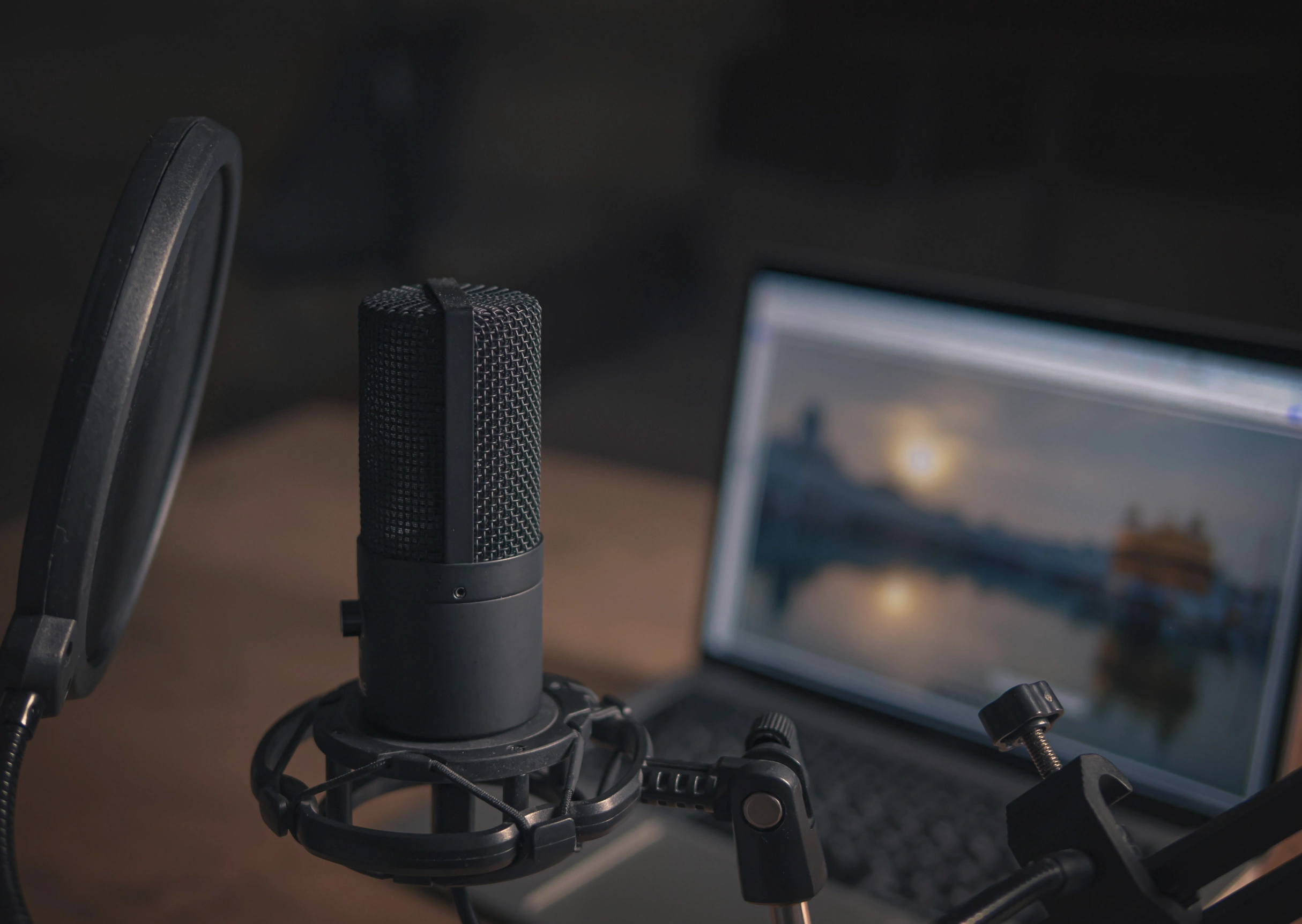 Studio microphone with pop filter in front of a laptop, set up for podcast recording.