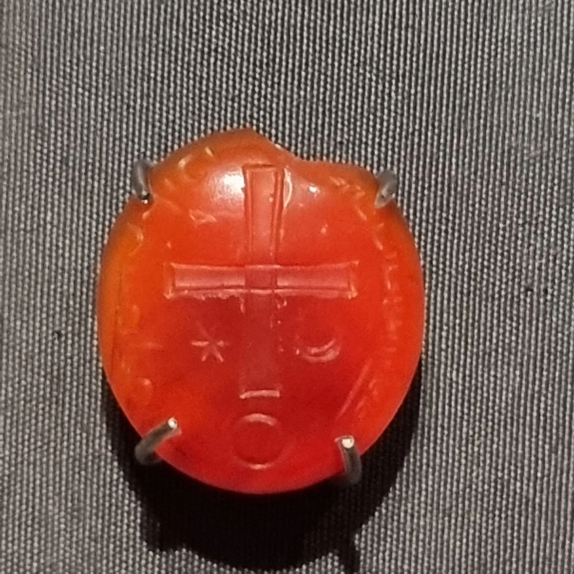 Red circular historical object with cross-like markings displayed against a dark textile surface.